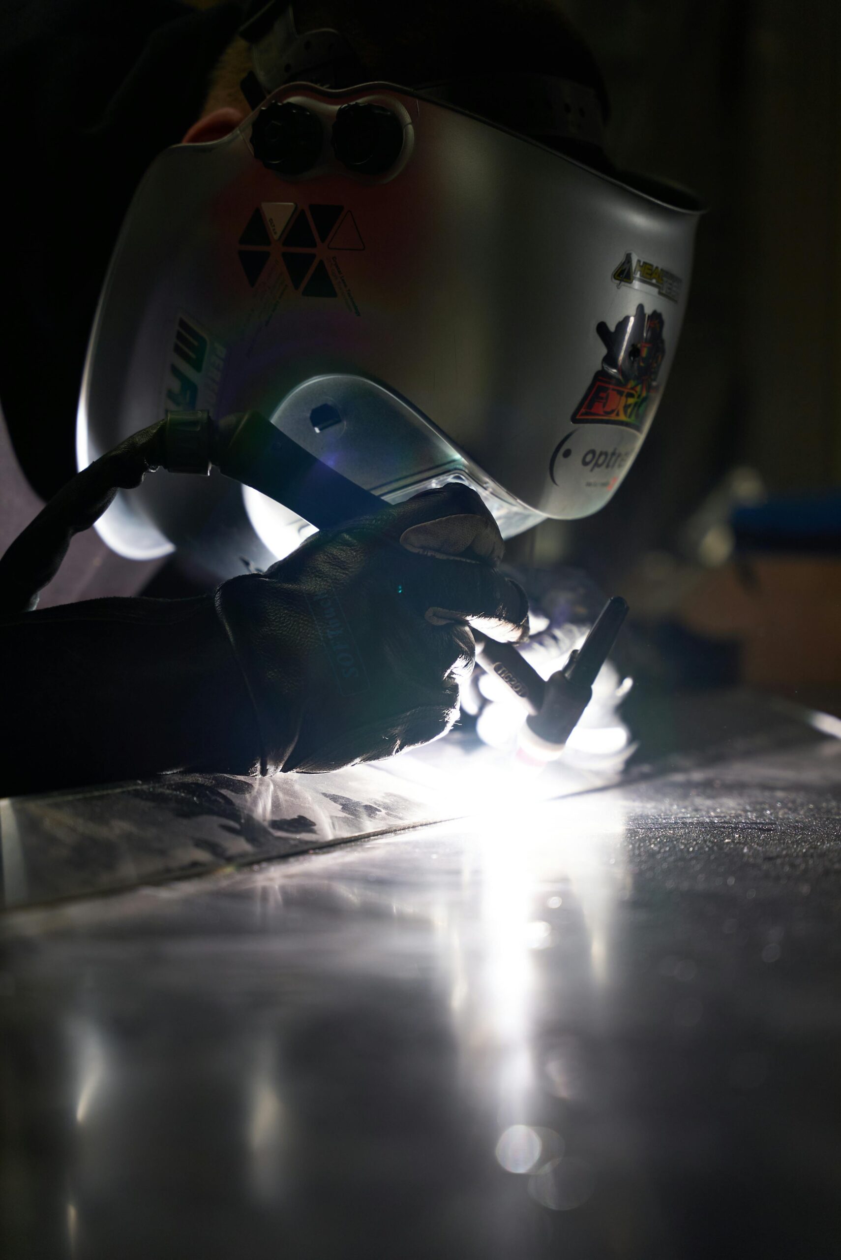 Close-up of a welder in action, wearing protective gear and welding metal indoors.